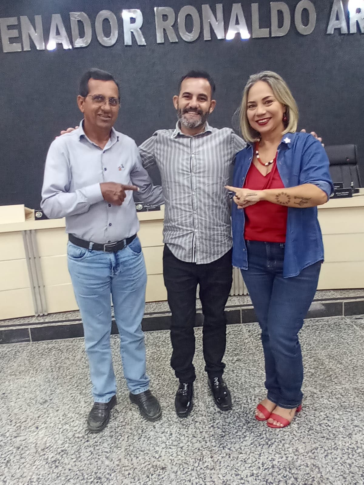 Dasilva ao centro, ao lado de duas pessoas diante de um painel.
